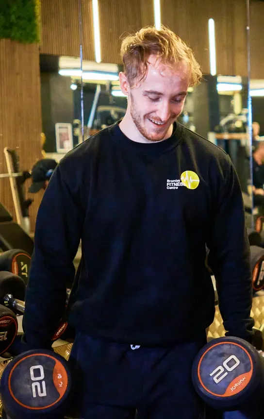 Coach selecting dumbbells at the free-weights rack at Avoya Fitness