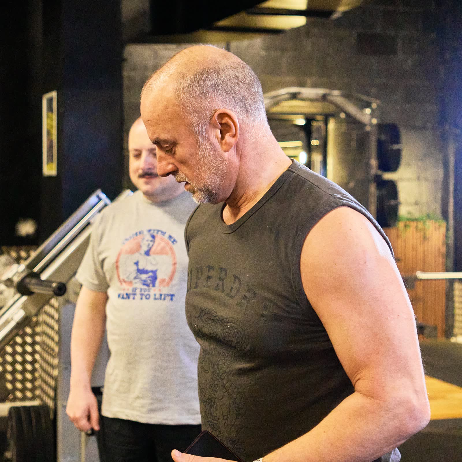 Member reviewing his programme on a phone with his coach beside him on the gym floor