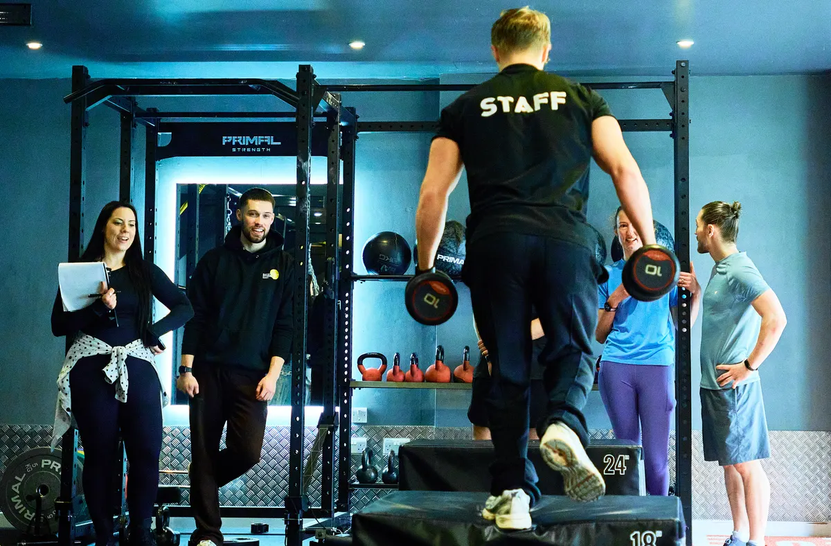 An Avoya coach demonstrating weighted box step-ups while members and coaches look on