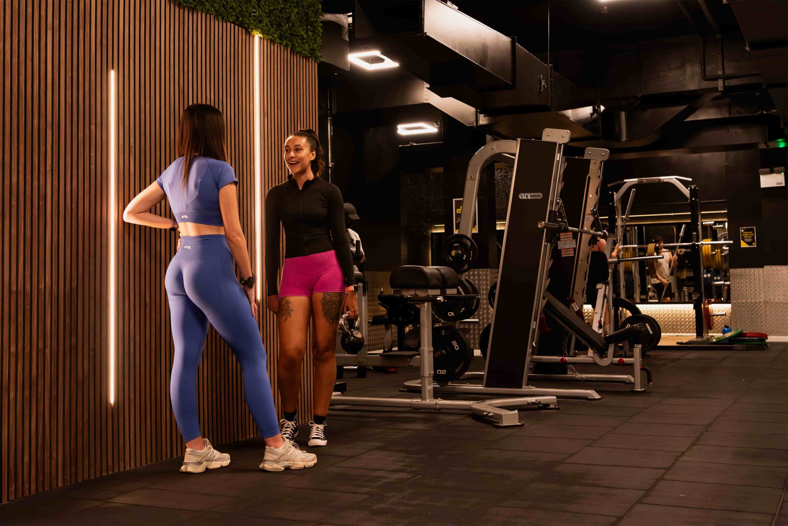 An Avoya coach sharing a laugh with a member at the free-weights rack in Bromley