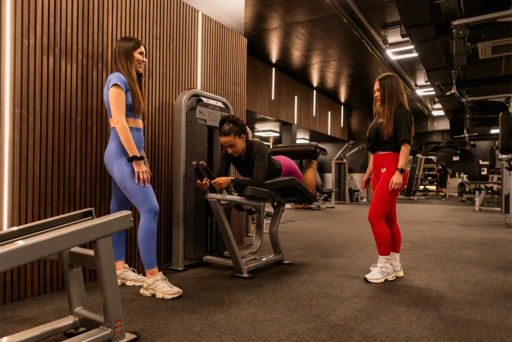 Personal trainer assisting a woman working out on a strength training machine.